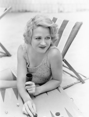 Young woman sitting at the beach playing backgammon clipart