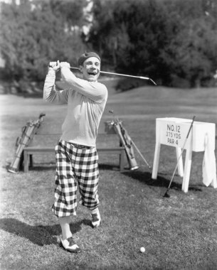 Man in knickerbockers swinging a golf club clipart