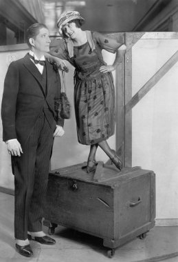 Woman standing on a trunk next to a very tall man