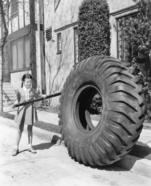 Girl playing with a huge tire and stick clipart