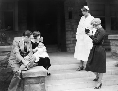 Parents with their new baby in front of the hospital being photographed clipart