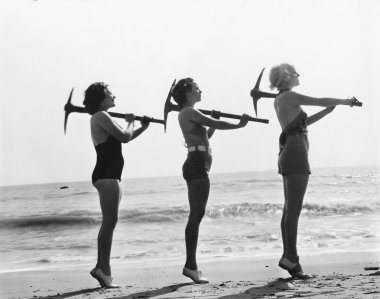 Three women posing with a pick ax on the beach clipart