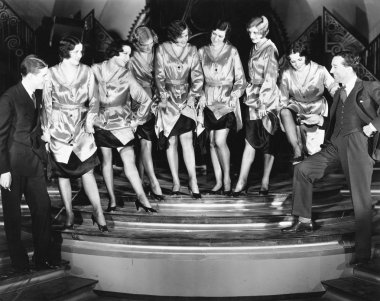 A chorus line of women showing off their legs to two men clipart