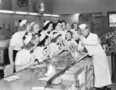 Young man surrounded by a group of college women in his soda fountain clipart