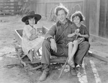 Father sitting with his two daughters on a small wagon on a farm clipart