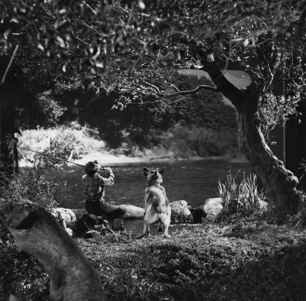 Garçon pêche avec chien dans la rivière — Photo