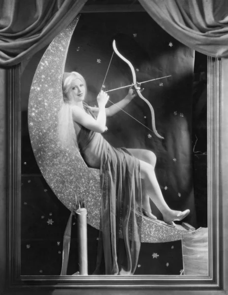 Woman sitting on crescent moon with bow and arrow — Stock Photo, Image