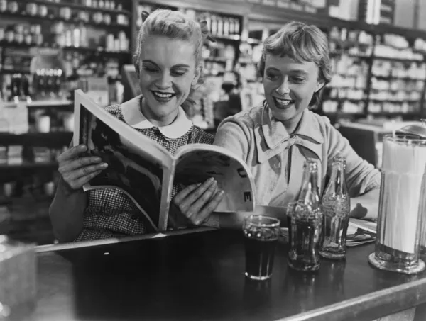 Freundinnen schauen sich Magazin am Limonadenbrunnen an — Stockfoto