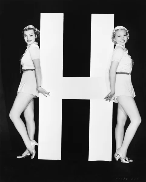 Женщины, позирующие с огромной буквой H — стоковое фото