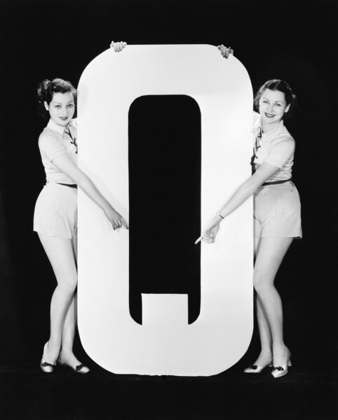 Two women pointing at huge letter Q