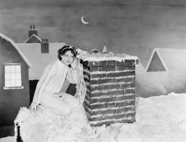 Mujer joven escuchando en la chimenea en el techo cubierto de nieve —  Fotos de Stock