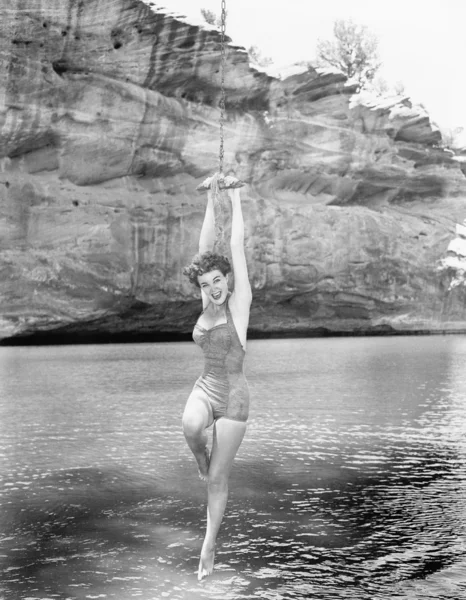 Woman hanging from rope swing over water — Stock fotografie
