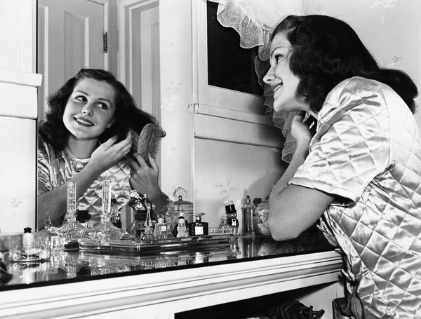 Mujer joven cepillando el cabello en el tocador — Foto de Stock