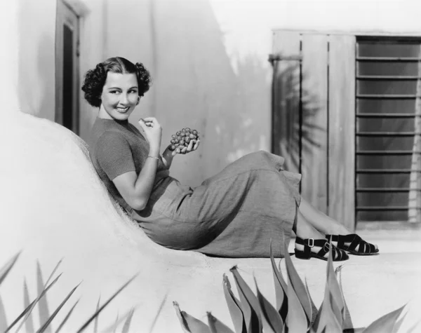 Mujer joven sentada en una terraza sonriendo y comiendo uvas —  Fotos de Stock