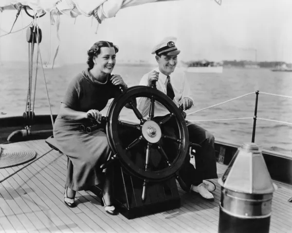 Casal sentado no convés de um veleiro dirigindo o barco — Fotografia de Stock