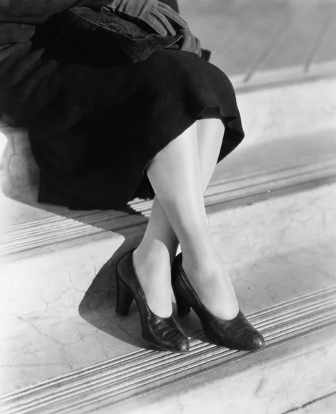 Τα πόδια μιας νεαρής γυναίκας με ψηλά τακούνια κάθονται σε ένα σκαλοπάτι — Φωτογραφία Αρχείου
