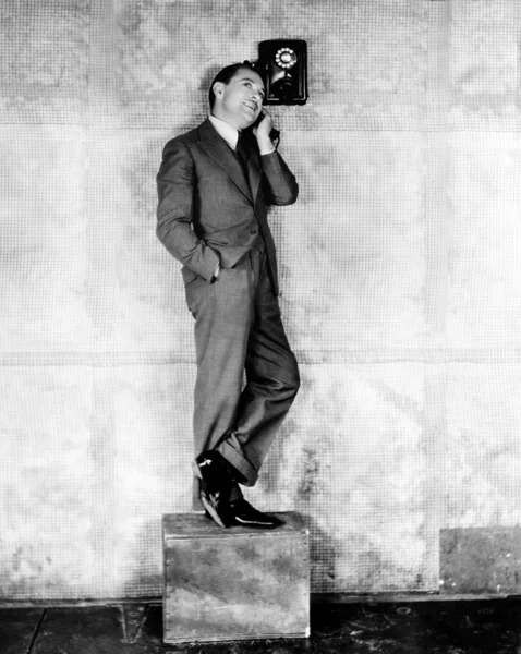 Homem de pé em uma caixa para chegar ao telefone — Fotografia de Stock