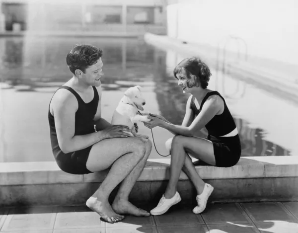 Pár sedí se svým štěňátkem u bazénu — Stock fotografie