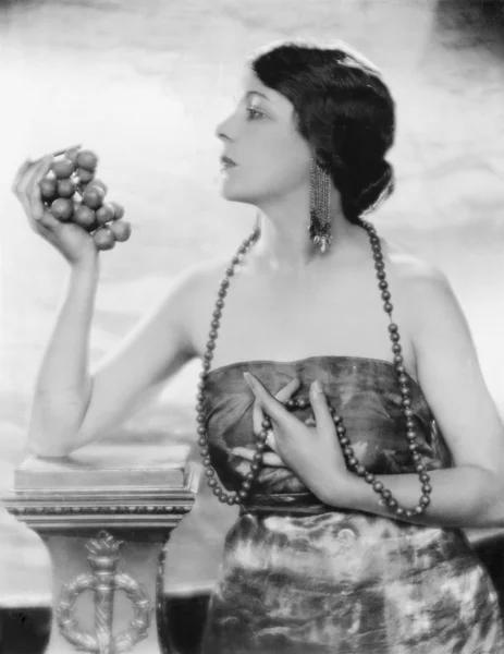 Mujer joven en perlas y vestido elegante sosteniendo y mirando las uvas — Foto de Stock