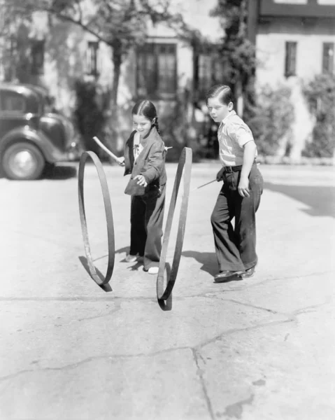 Garçon et fille jouer cerceau et bâton sur un trottoir — Photo
