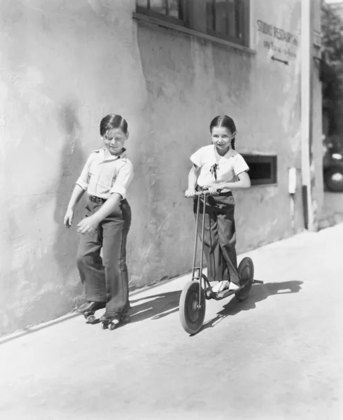 Мальчик и девочка играют на скутере, а другой на роликах — стоковое фото