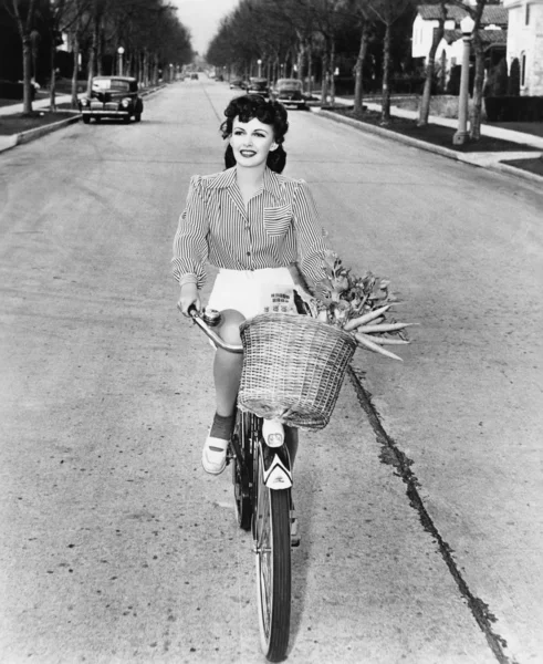 Mladá žena, jezdit na kole s košíkem květin a mrkev — Stock fotografie