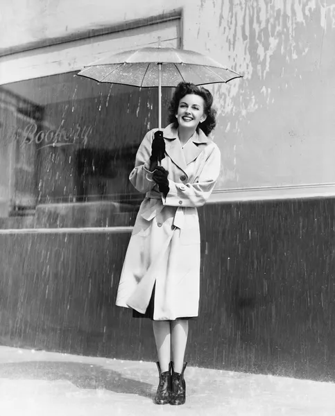 Молодая женщина в плаще и зонтике стоит под дождем — стоковое фото
