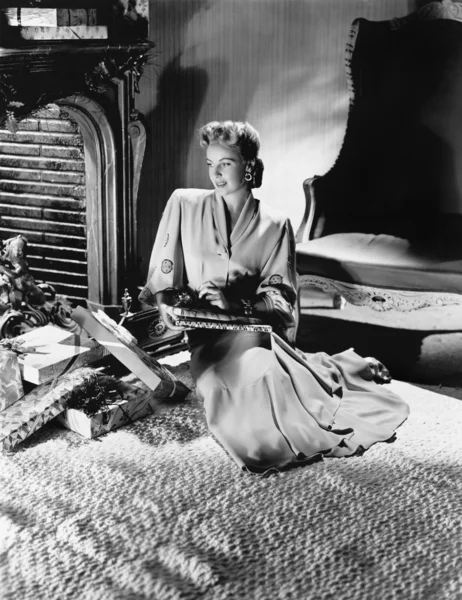 Молодая женщина в элегантном платье сидит на кровати с большим количеством подарков вокруг нее — стоковое фото