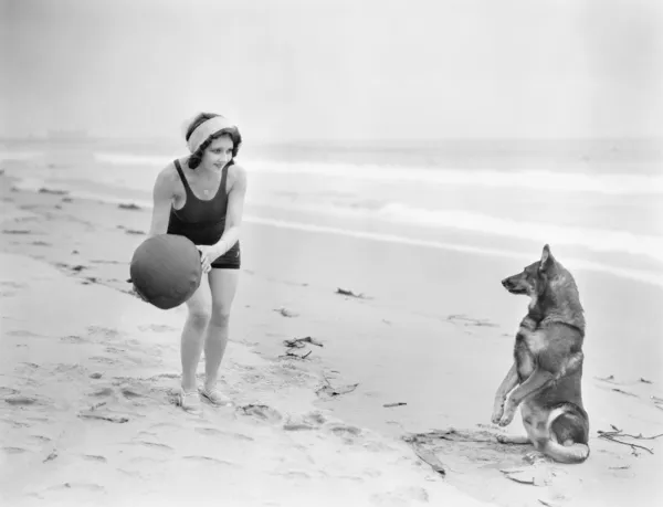 Jovem mulher brincando com seu cão e bola na praia — Fotografia de Stock