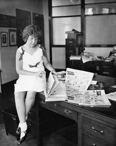 Dziewczyna siedzi na biurku i czytanie gazety — Zdjęcie stockowe