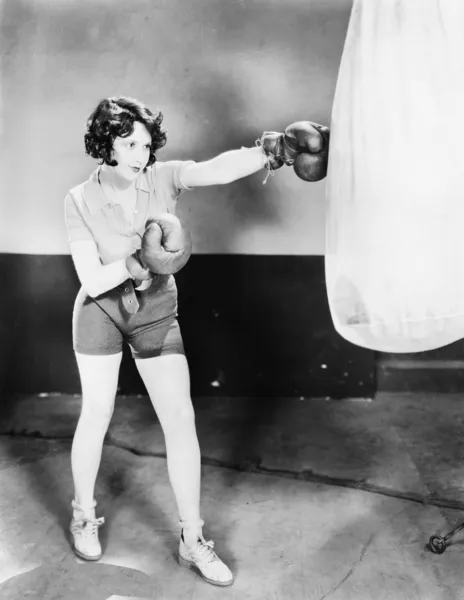 Mujer joven con guantes de boxeo entrena con un saco de boxeo —  Fotos de Stock