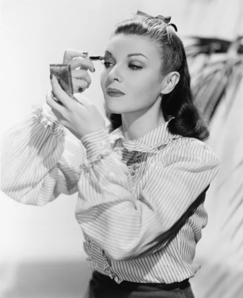 Jovem mulher olhando para um espelho e vestindo maquiagem — Fotografia de Stock