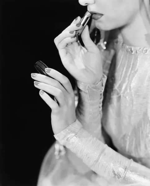 Mujer joven mirando en un espejo y maquillándose — Foto de Stock