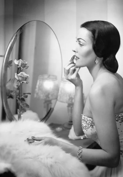 Jovem mulher olhando para um espelho e vestindo maquiagem — Fotografia de Stock