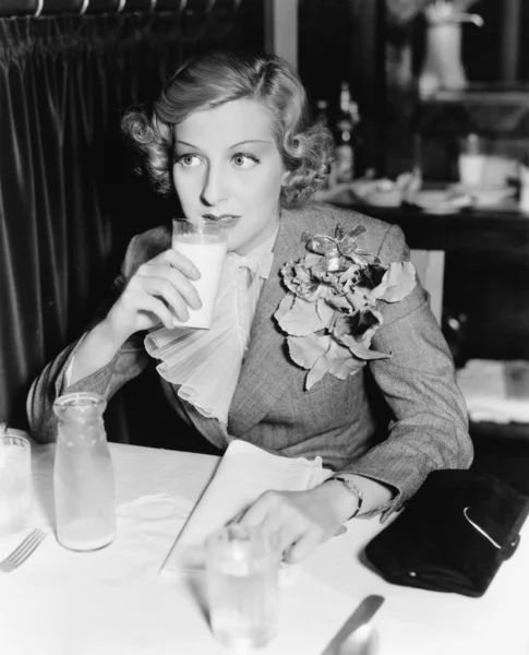 Jovem mulher sentada a uma mesa em um restaurante bebendo leite — Fotografia de Stock