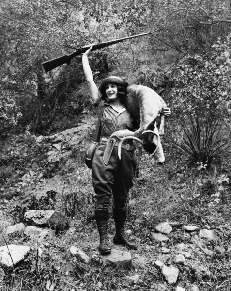 Oh veado, uma jovem caçadora com arma levantada sorrisos altos com um jovem fanfarrão na mão — Fotografia de Stock