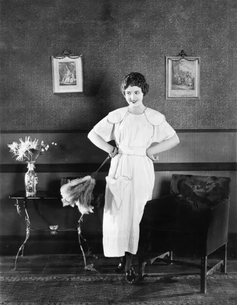 Bir önlük ve oturma odasında bir toz bezi duran genç kadın — Stok fotoğraf