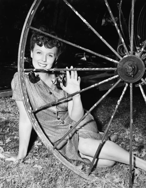 Jovem mulher sorrindo enquanto se senta atrás de uma roda de vagão — Fotografia de Stock