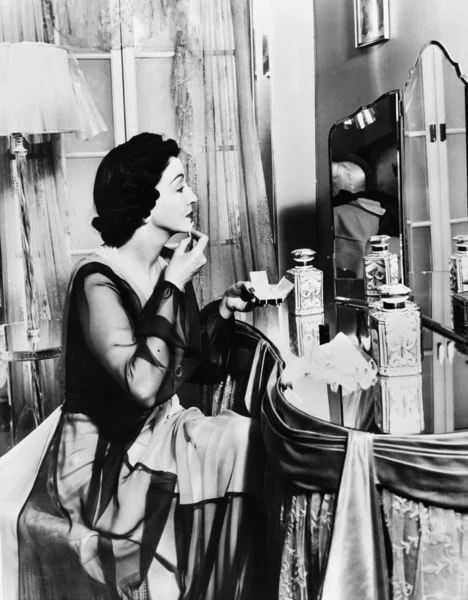 :Jovem mulher olhando para um espelho e vestindo maquiagem — Fotografia de Stock