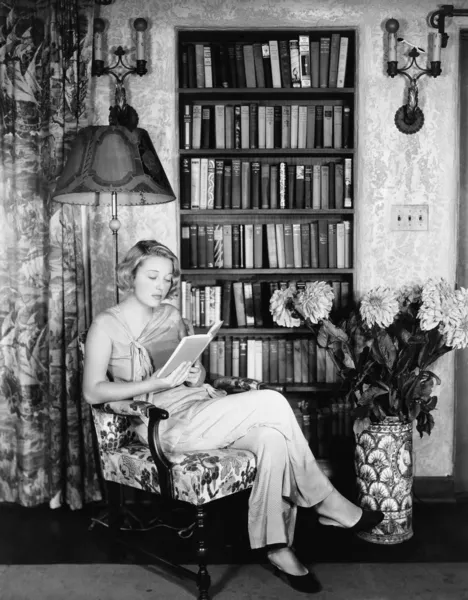 Ung kvinna läser i hennes bibliotek — Stockfoto