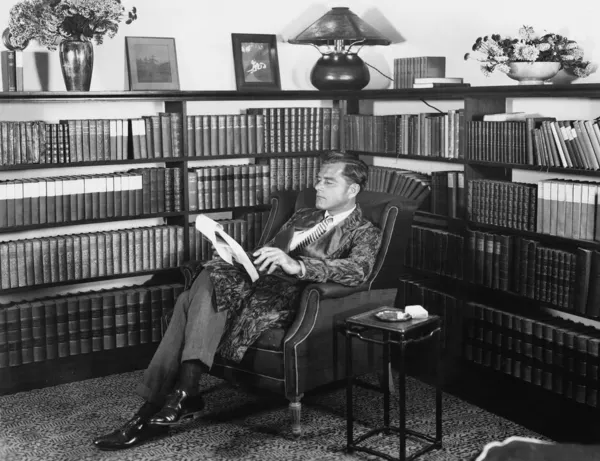 Hombre sentado en su biblioteca leyendo un libro —  Fotos de Stock