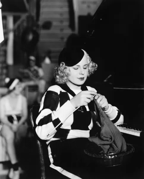 Young woman sitting and knitting at piano — Stock Photo, Image
