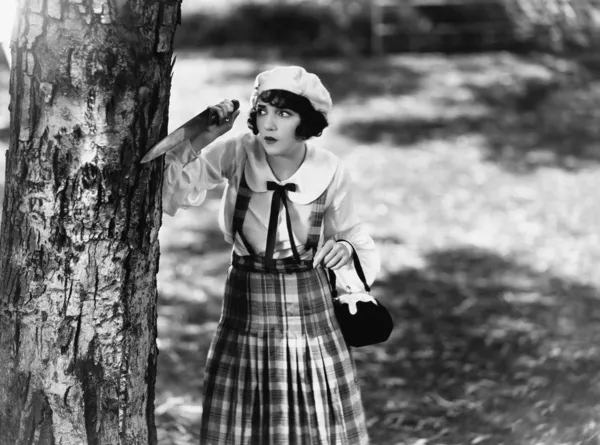Νεαρή γυναίκα με ένα μαχαίρι περιμένει πίσω από ένα δέντρο — Φωτογραφία Αρχείου