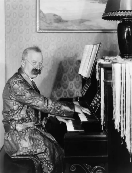 Mannen i en mantel som spelar hans piano i vardagsrummet — Stockfoto