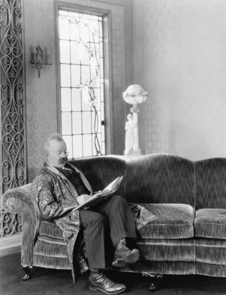 Человек сидит на диване и читает книгу — стоковое фото
