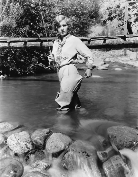 Kvinna med ett fiskespö stående i vattnet — Stockfoto