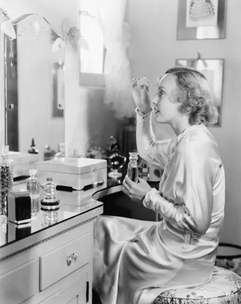 Mulher sentada na frente de sua vaidade colocando perfume em suas sobrancelhas — Fotografia de Stock
