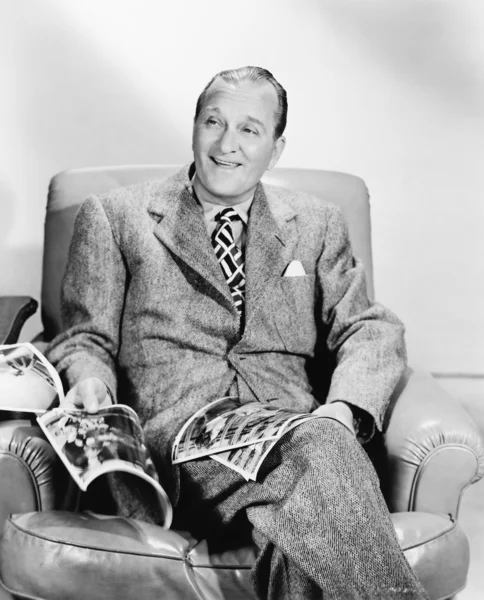Man sitting on an armchair reading a magazine — Stock Photo, Image