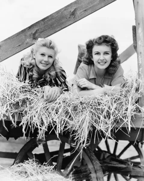 stock image Two women lying in a wagon of hay with their legs in the air