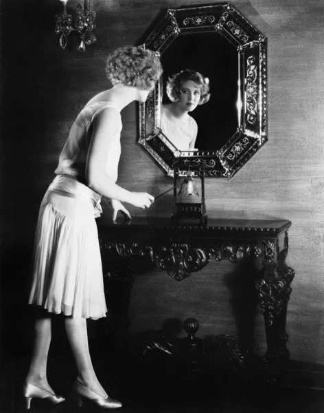 Mulher olhando em um espelho prestes a tocar um sino — Fotografia de Stock